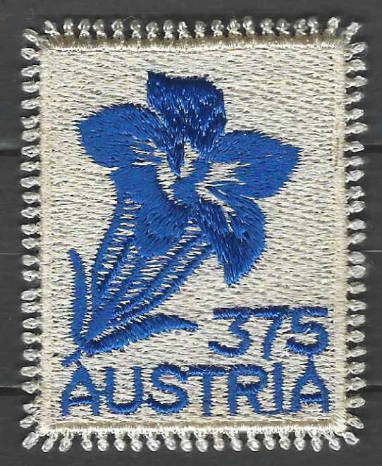 pašto ženklas, Austrija. Gėlė gencijonas. Siuvinėtas siūlais ant atlasinio audinio. Gaminamas individualiai. Su kutosais vietoj perforacijos